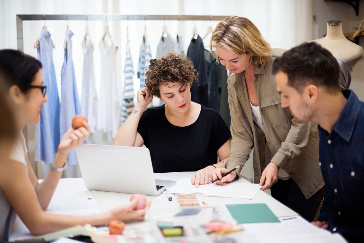 Apparel brand team reviewing designs and fabric swatches beside a clothing rack