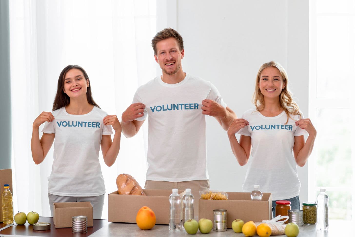 Three volunteers in matching printed VOLUNTEER tees at a donation table